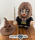 Toy character art with a female wizard next to a brown pointed hat on a wooden platform. 