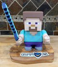 Toy figure of a character holding a sword on a wooden base against a stone wall background.
