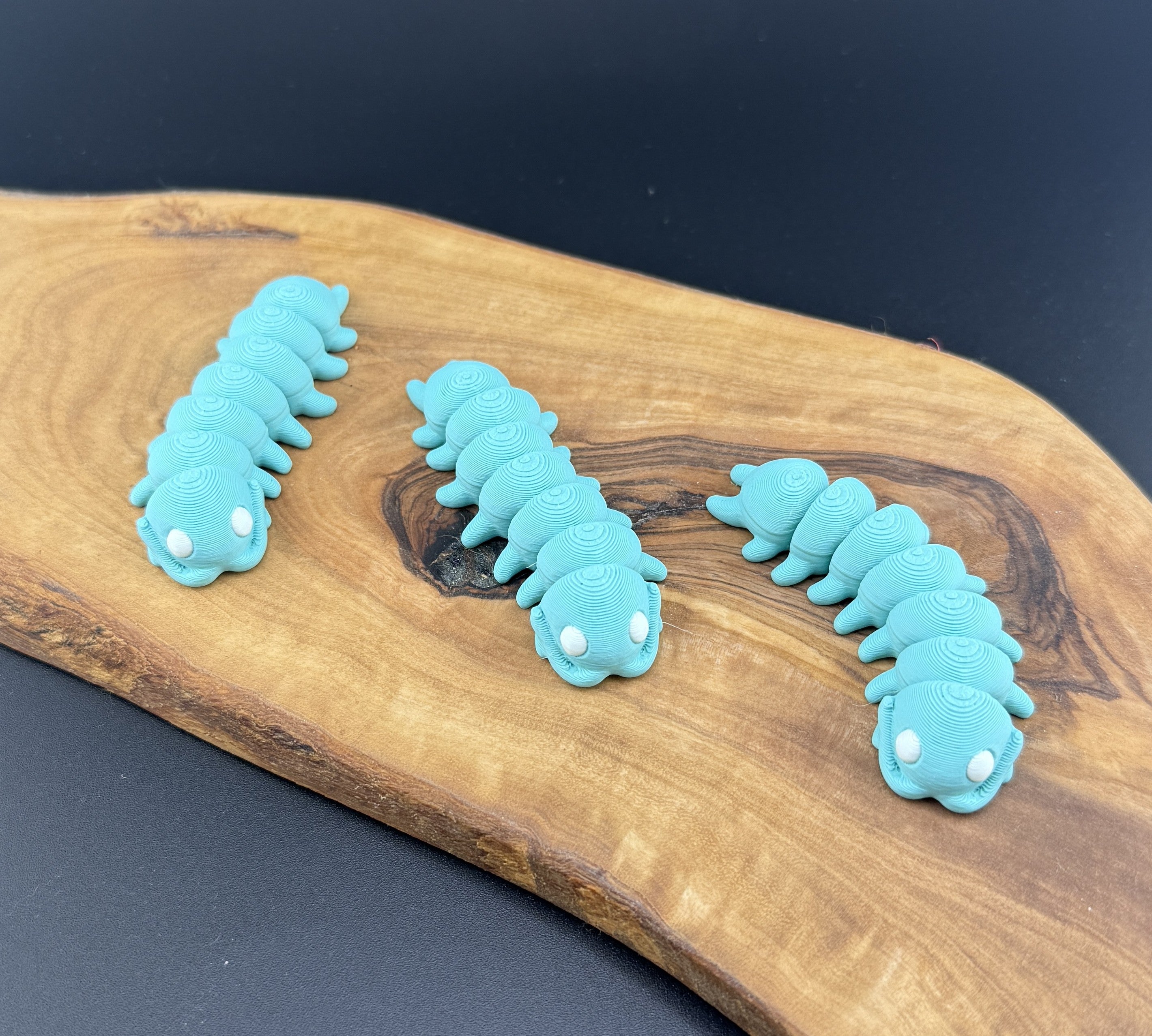 Three small fidget centipedes  on a wooden surface with a coin for scale.