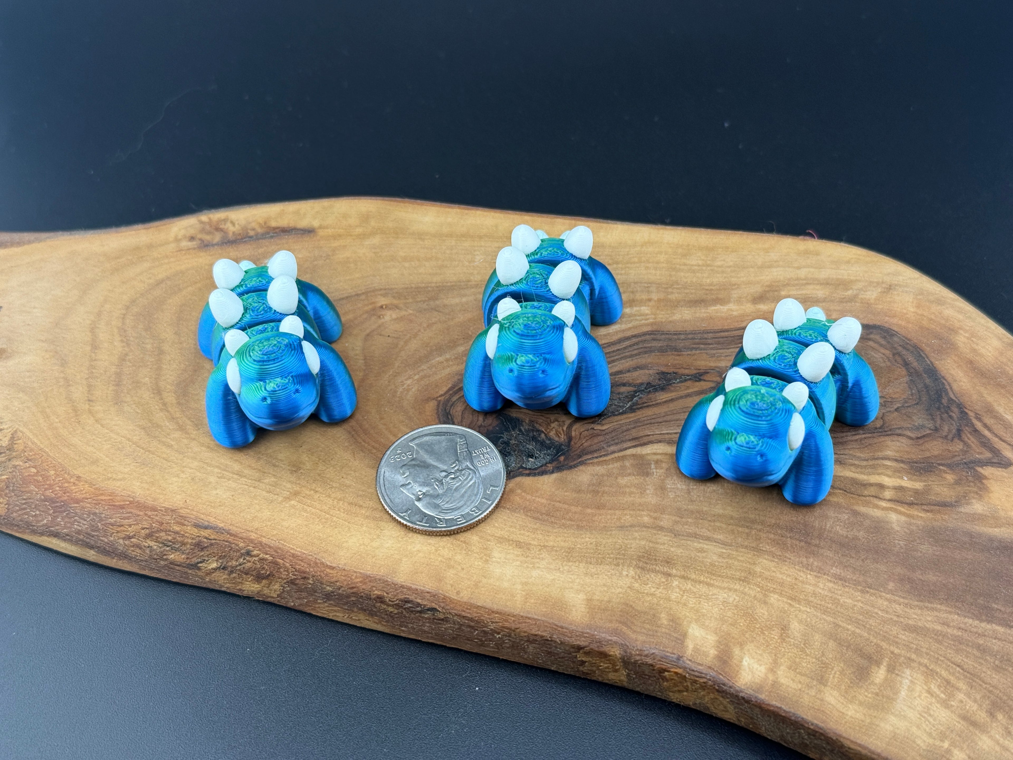 Three small fidget Stegosauruses  on a wooden surface with a coin for scale.