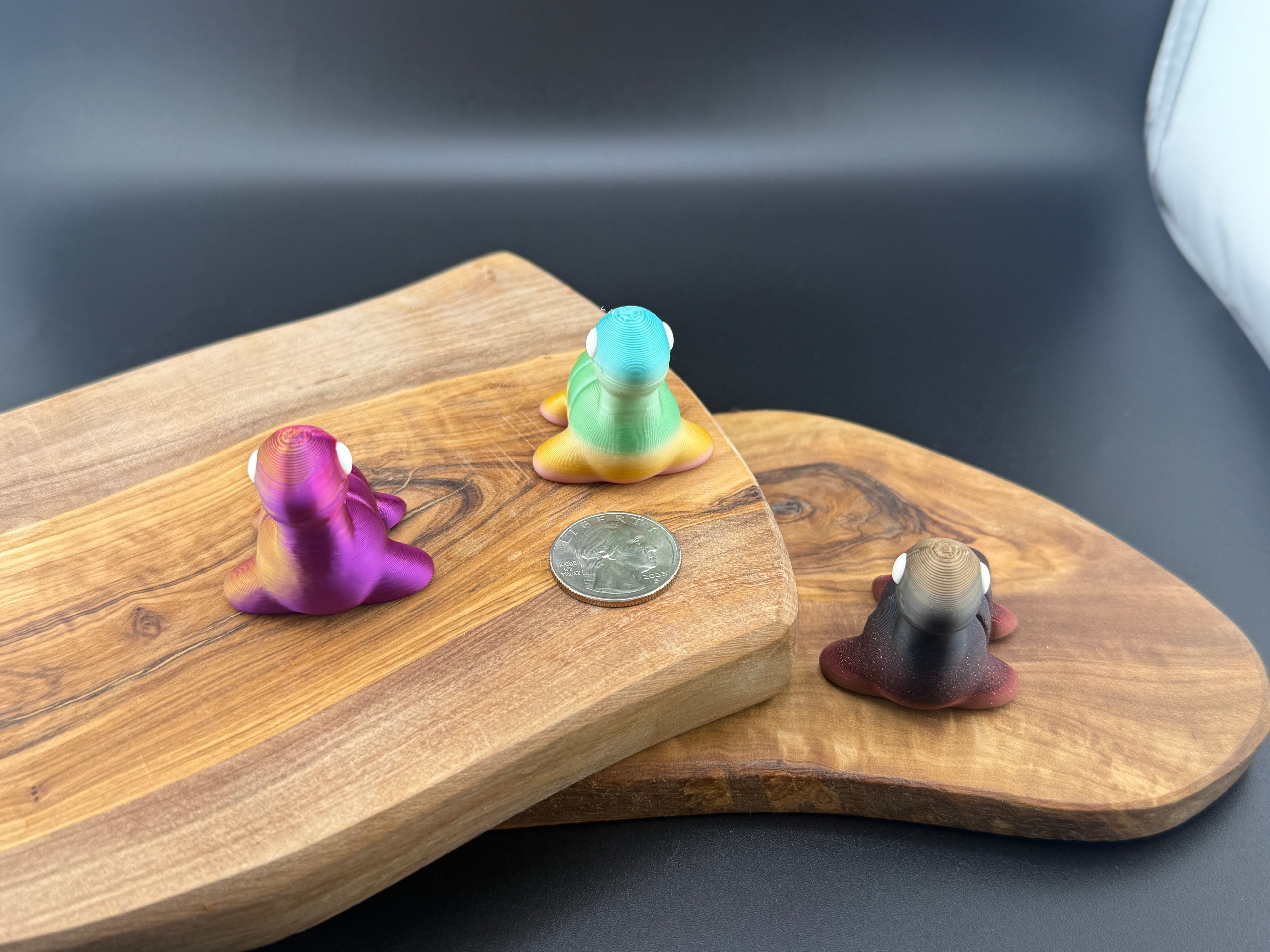 Three small fidget loch ness monsters  on a wooden surface with a coin for scale.