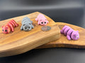 Three small fidget pigs  on a wooden surface with a coin for scale.