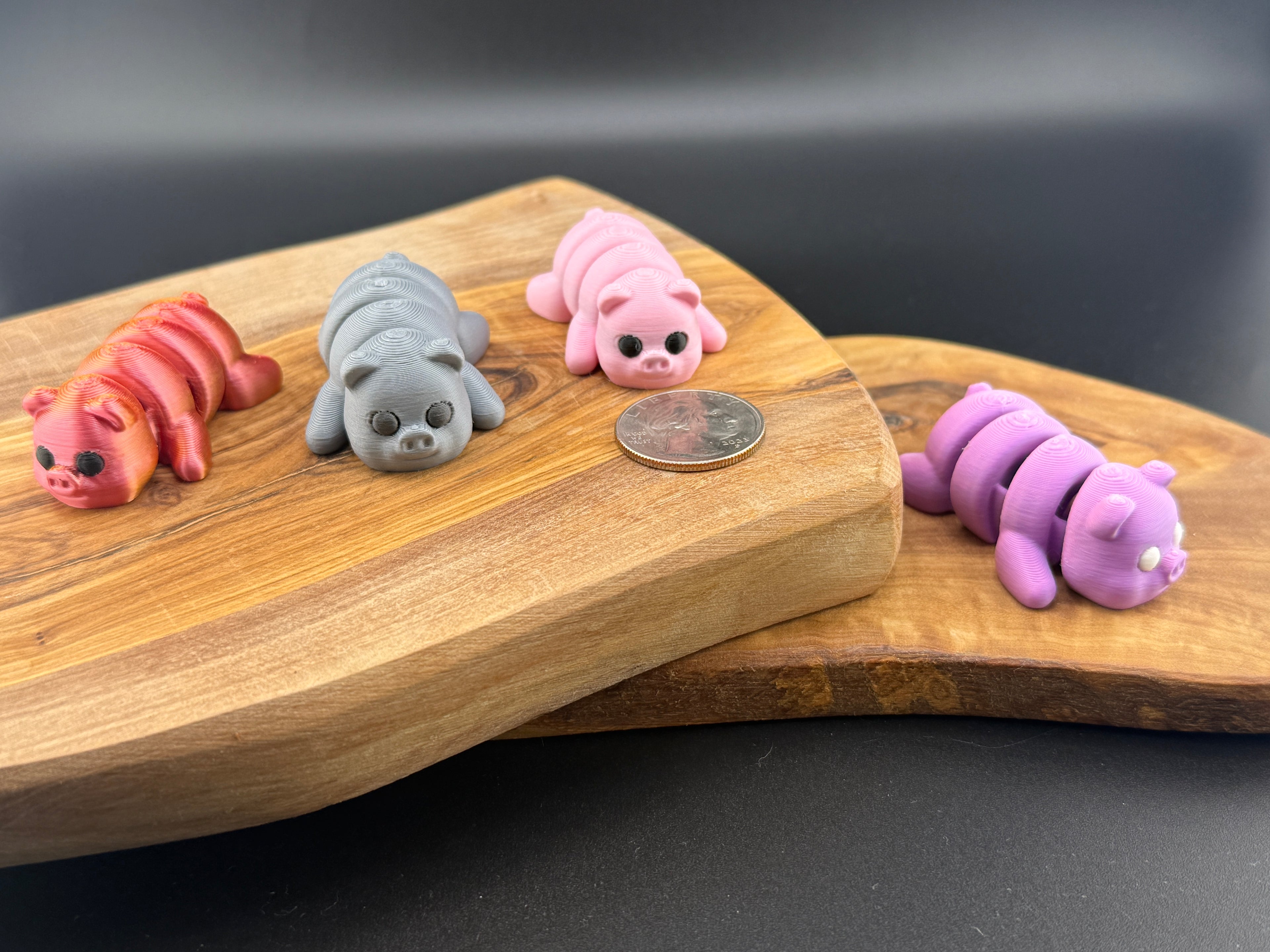 Three small fidget pigs  on a wooden surface with a coin for scale.