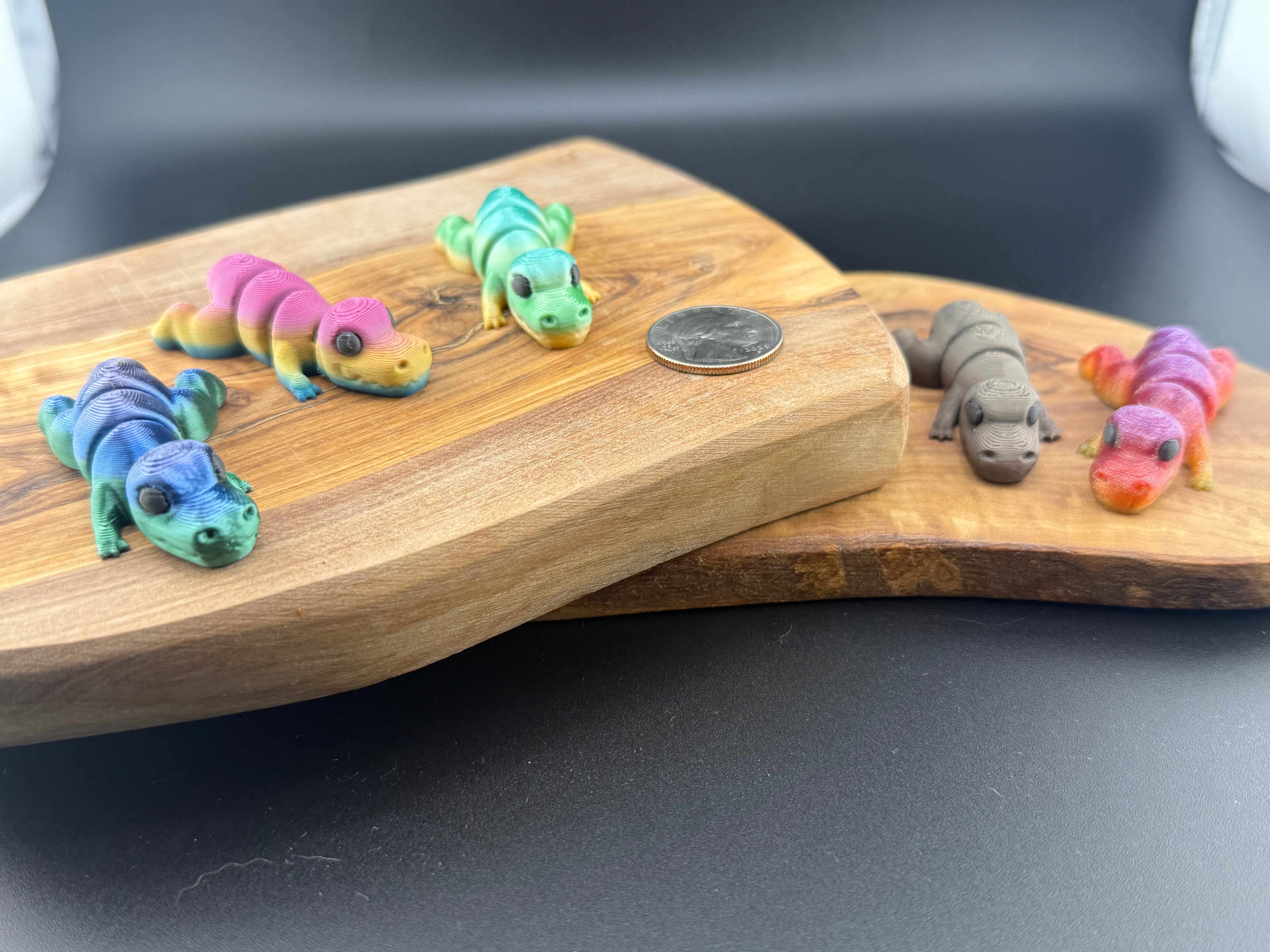 Three small fidget T Rexs  on a wooden surface with a coin for scale.