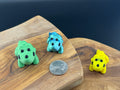 Three small fidget triceratops  on a wooden surface with a coin for scale.