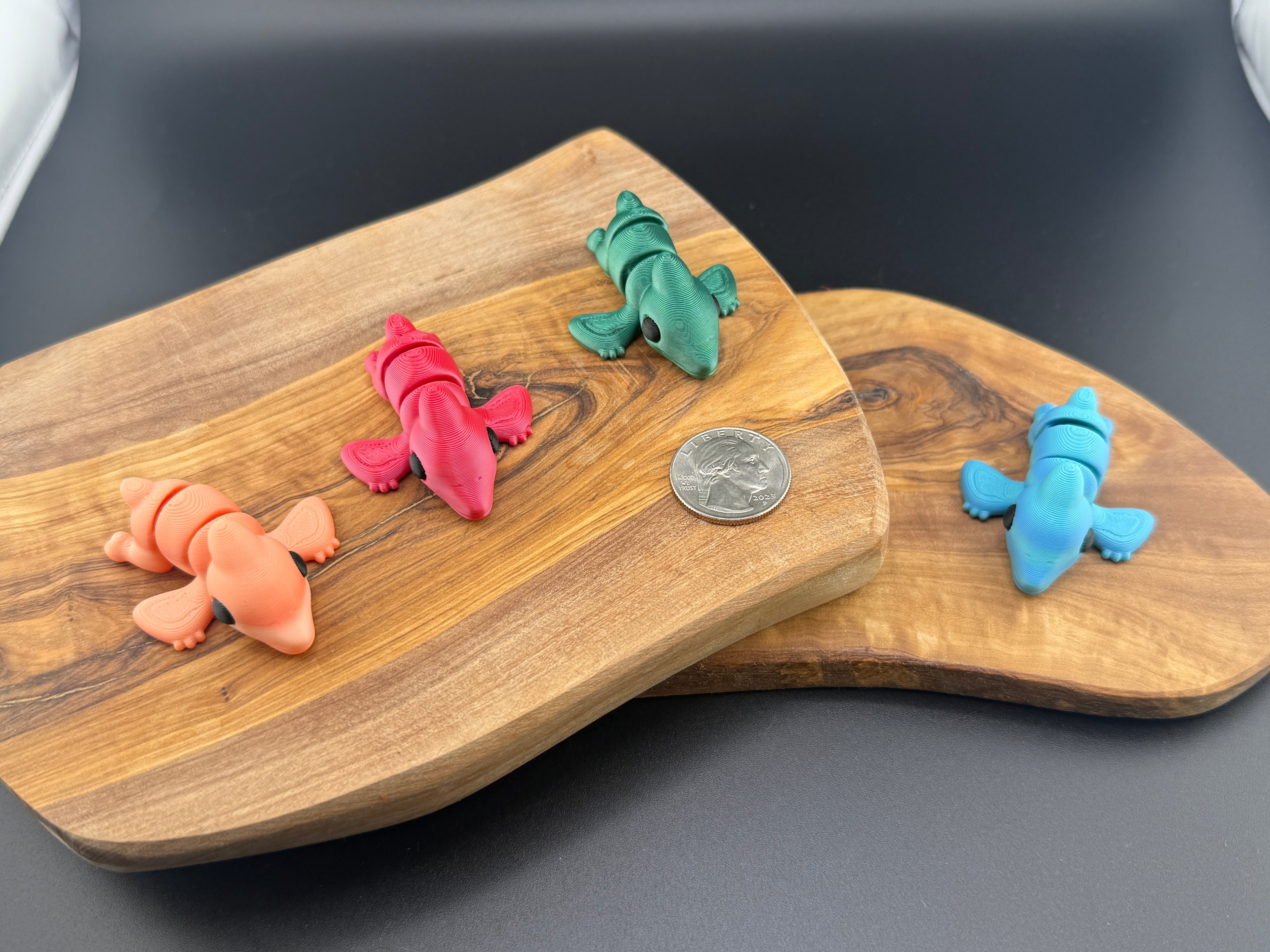 Three small fidget pteradactyls  on a wooden surface with a coin for scale.