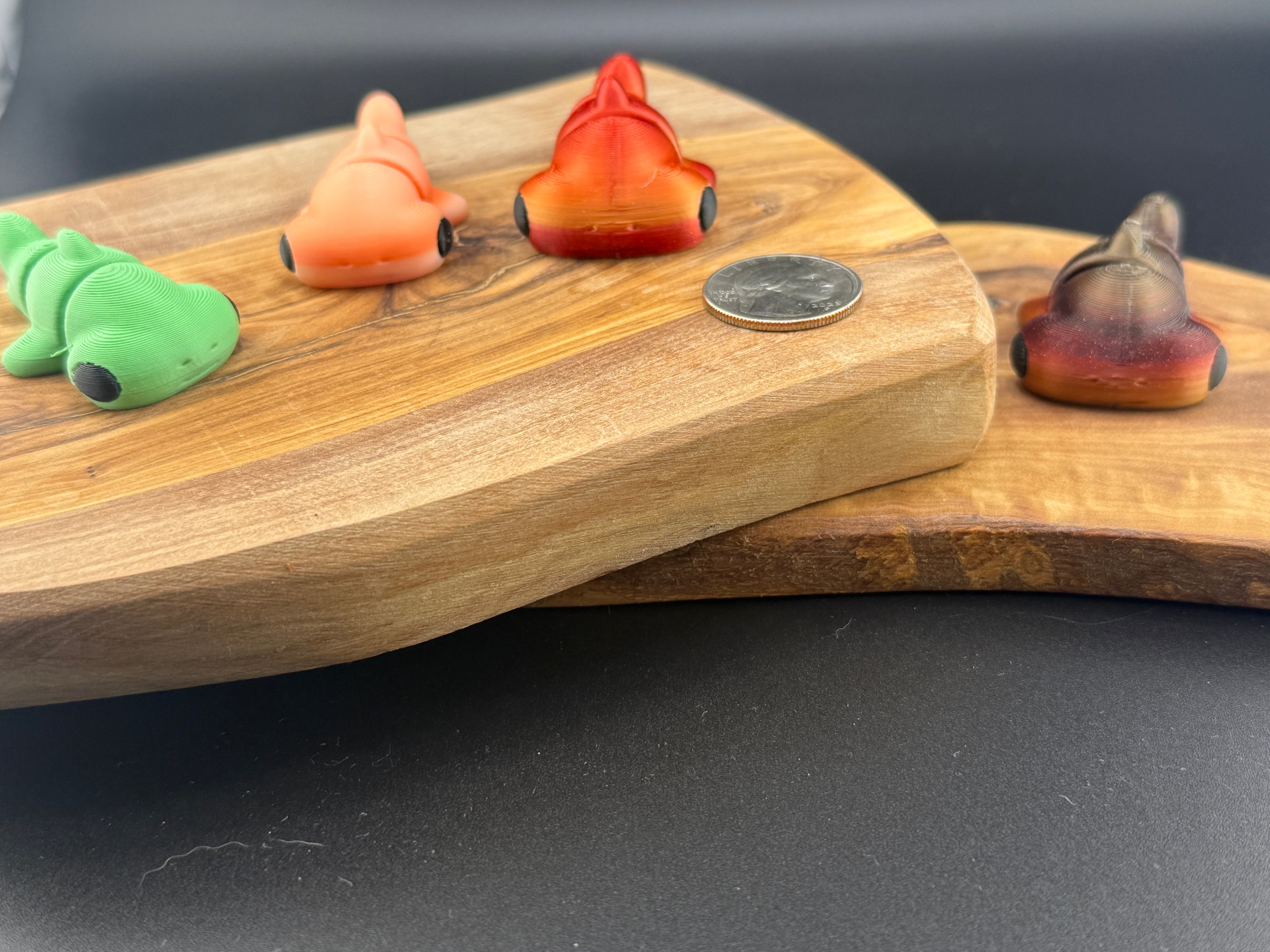 Three small fidget hammer head sharks  on a wooden surface with a coin for scale.