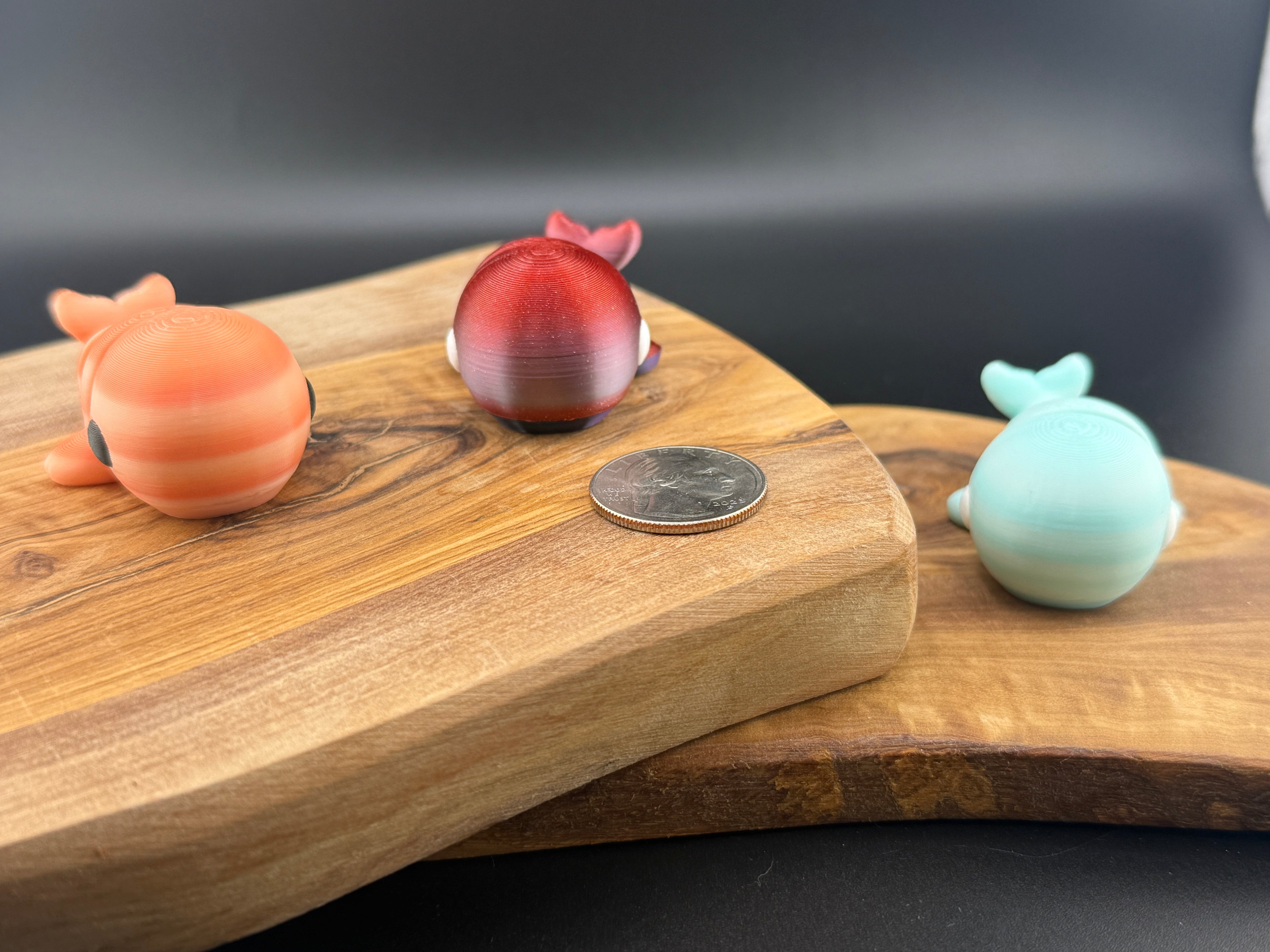 Three small fidget whales  on a wooden surface with a coin for scale.