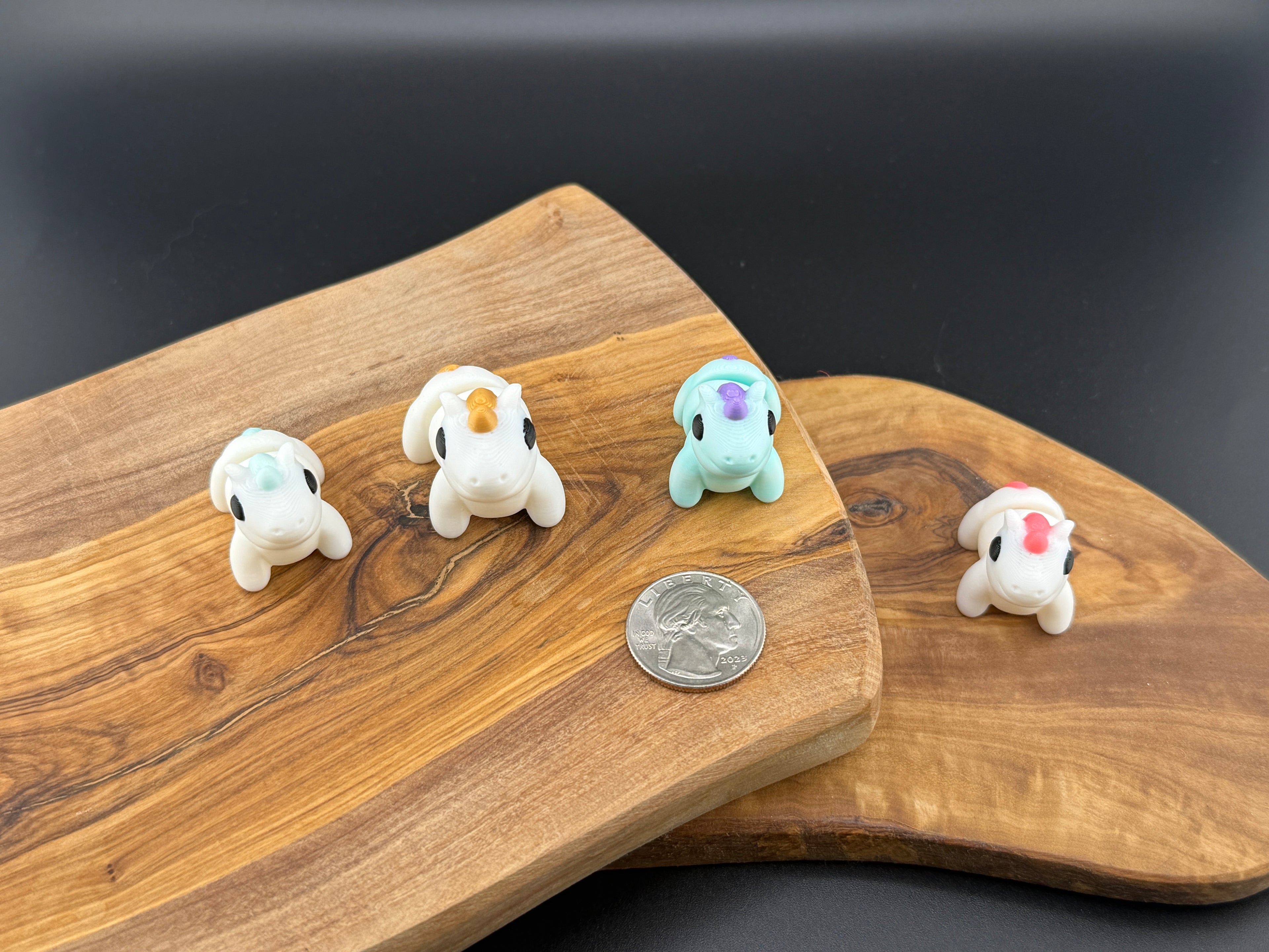 Four small fidget unicorns  on a wooden surface with a coin for scale.