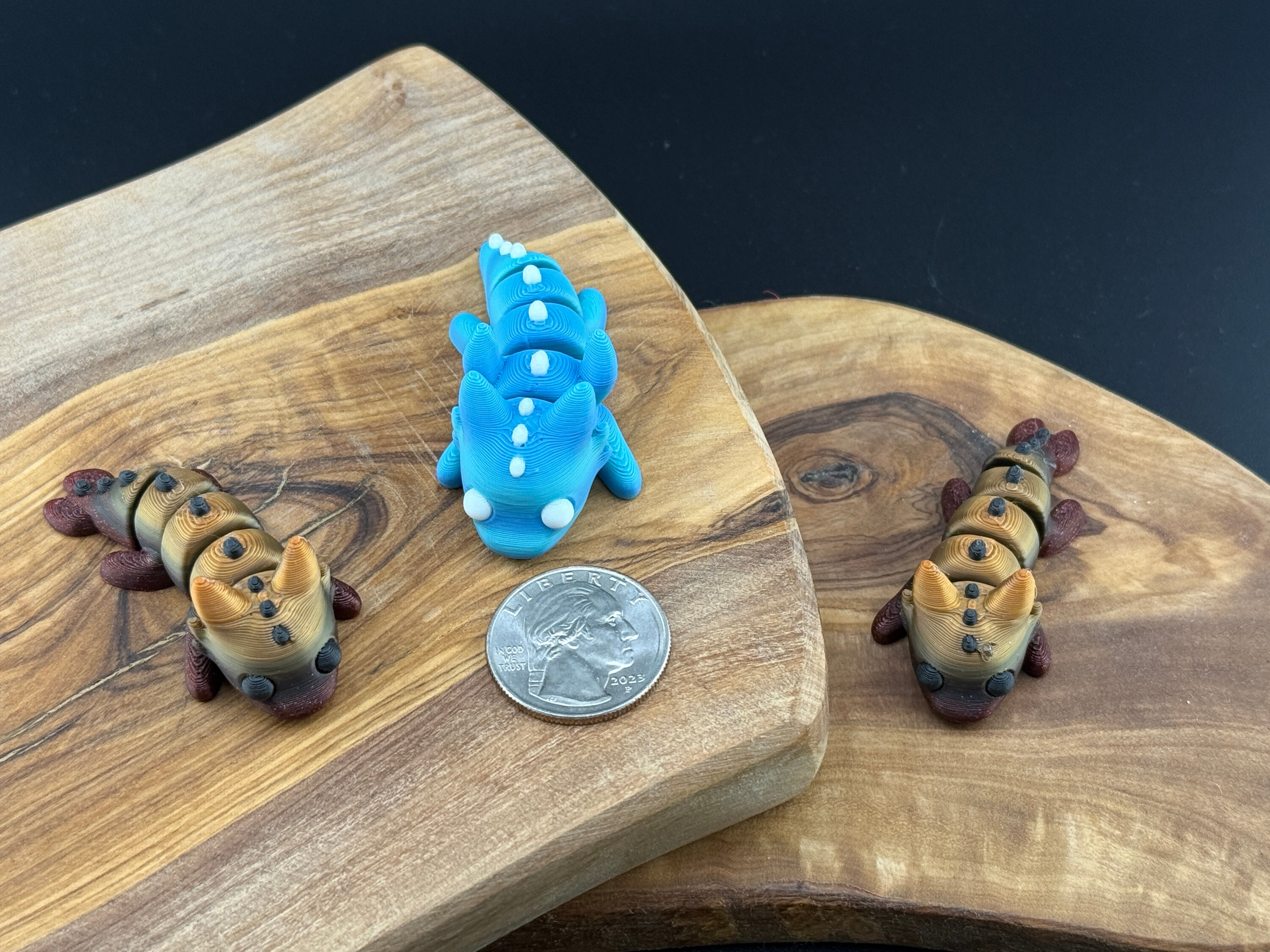 Three small fidget dragons  on a wooden surface with a coin for scale.