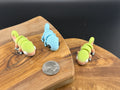 Three small fidget chameleons  on a wooden surface with a coin for scale.