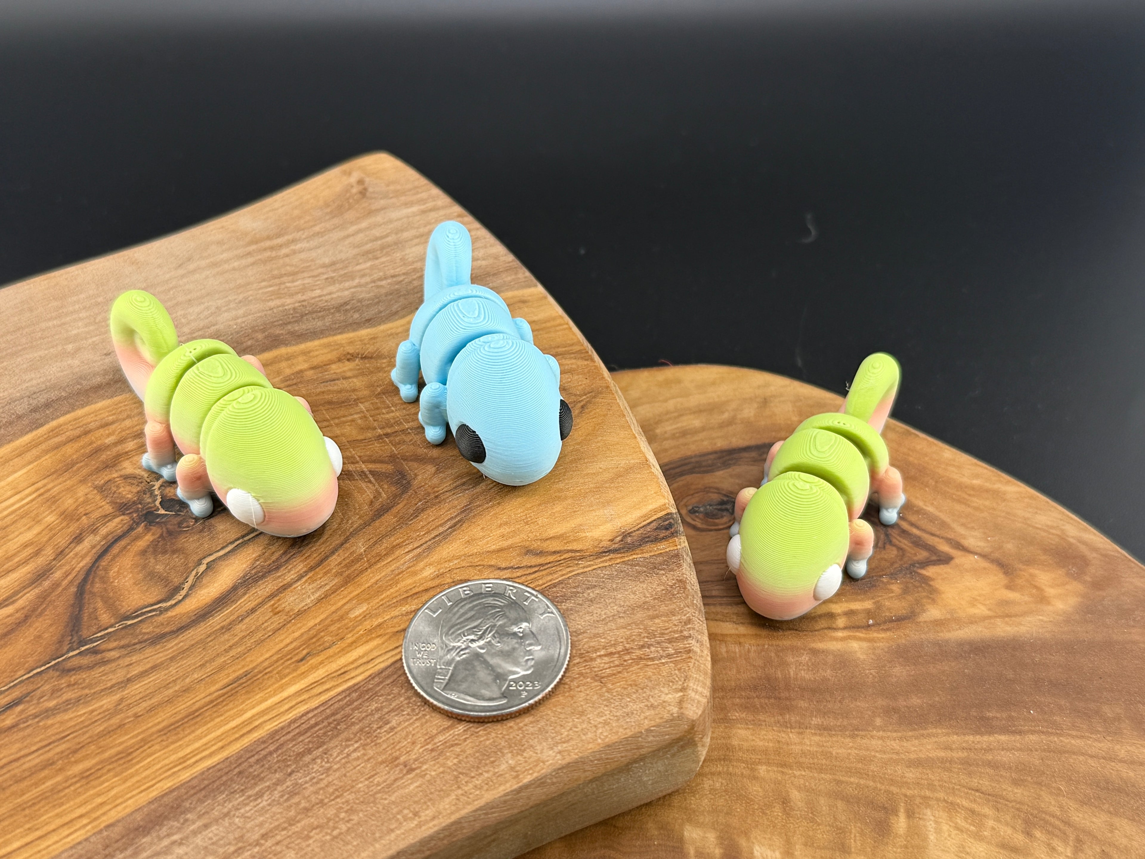 Three small fidget chameleons  on a wooden surface with a coin for scale.