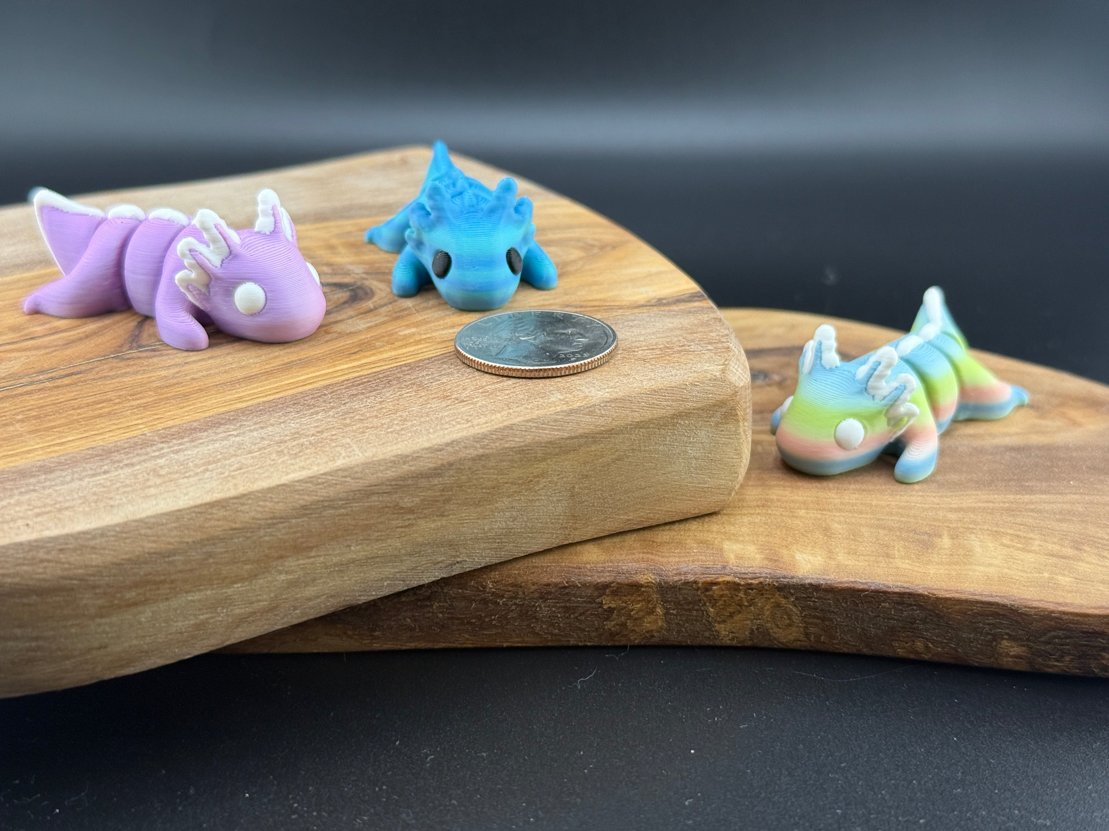 Three small fidget axolotls on a wooden surface with a coin for scale.