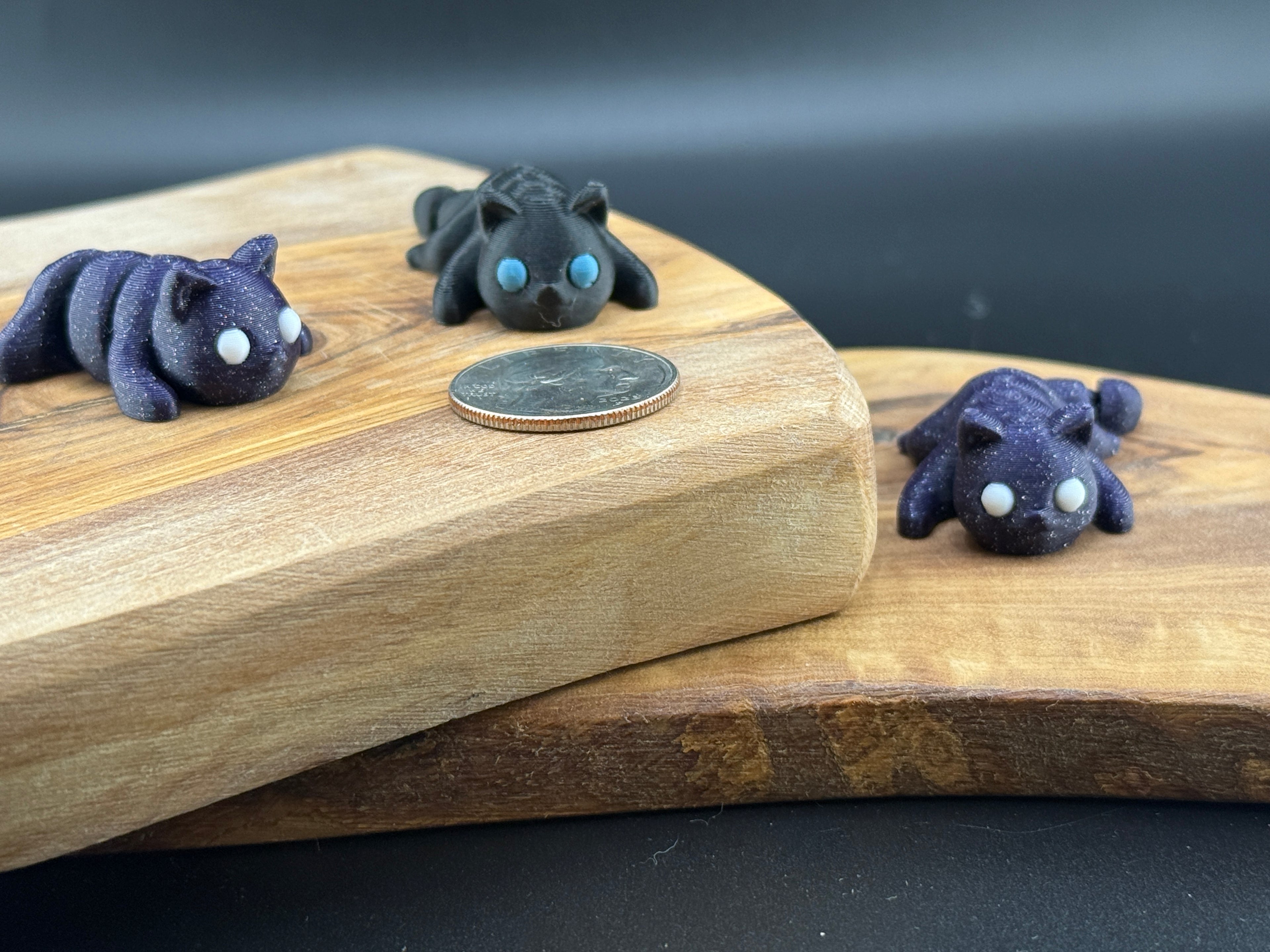 Three small fidget cats  on a wooden surface with a coin for scale.