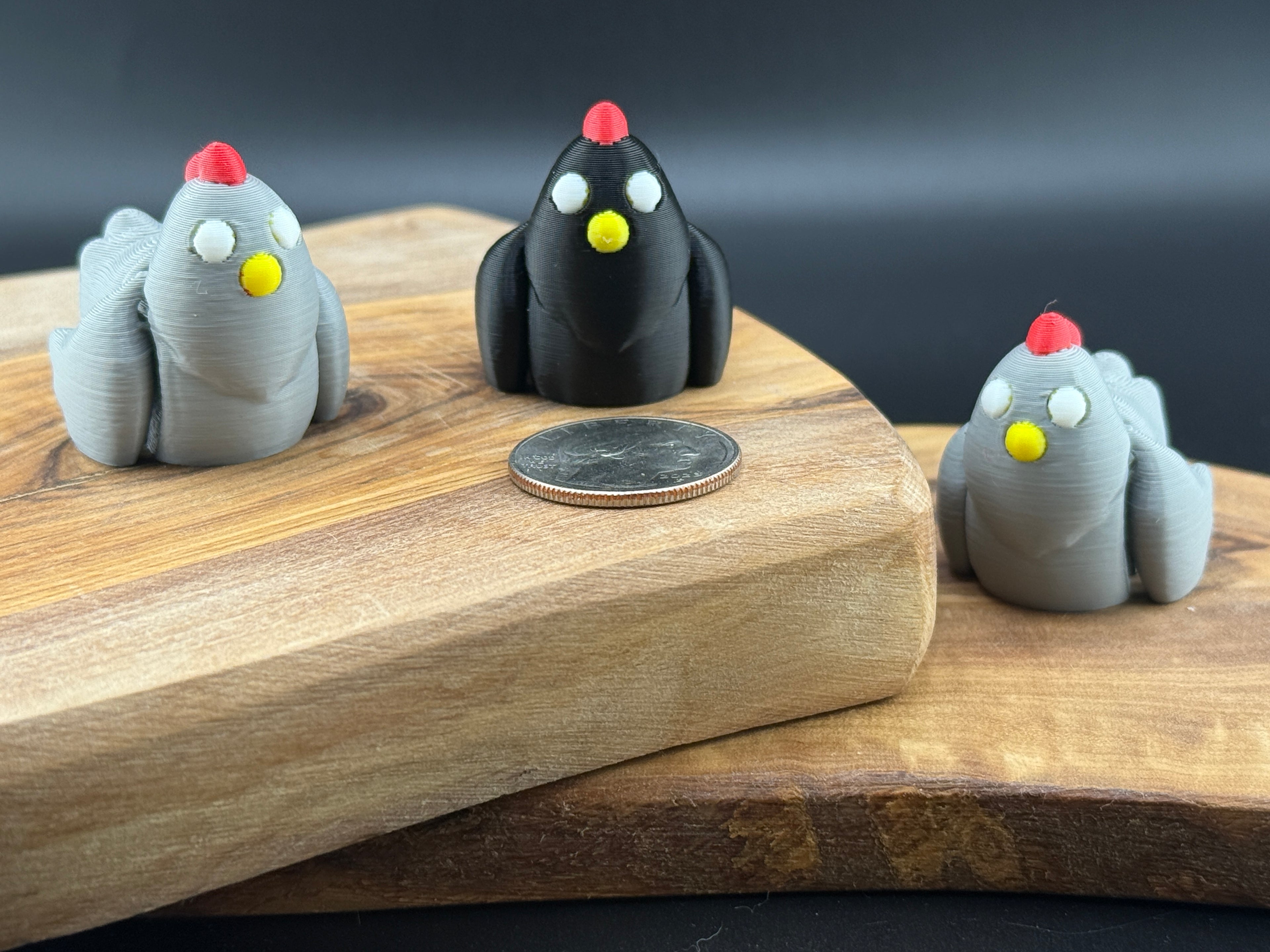Three small fidget chickens on a wooden surface with a coin for scale.