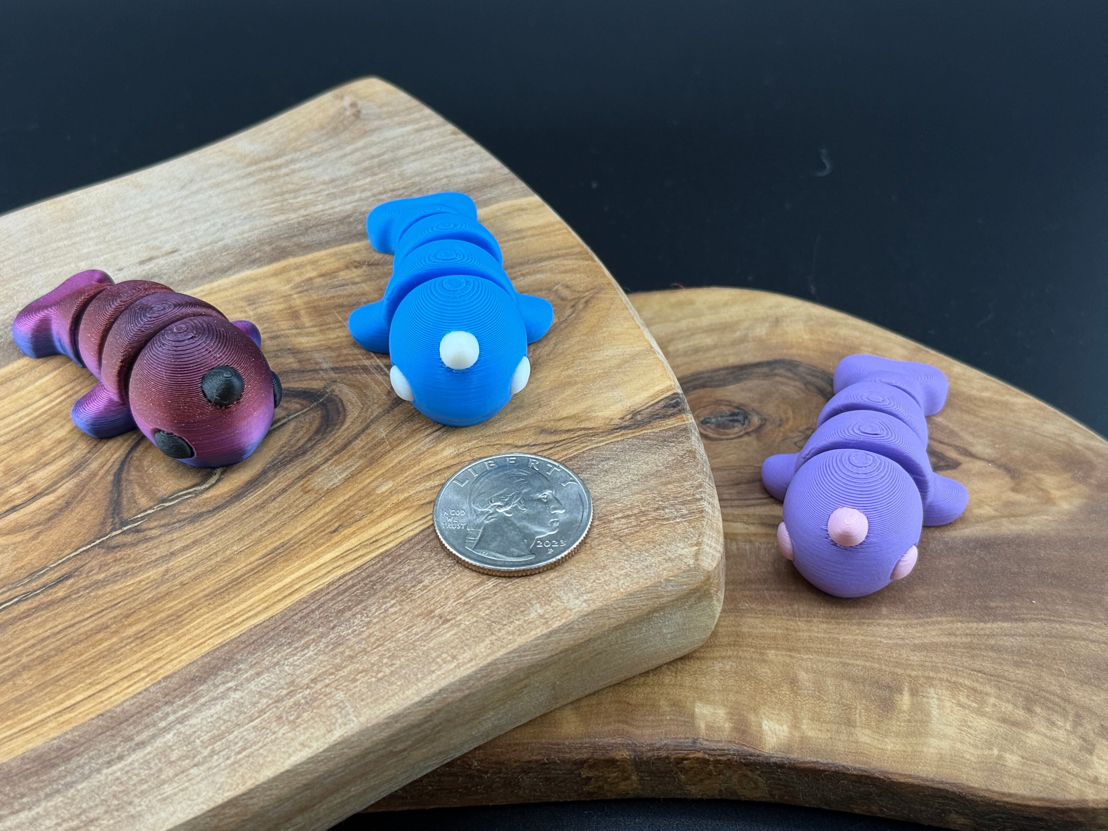 Three small fidget narwhal  on a wooden surface with a coin for scale.