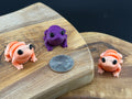 Three small fidget frogs on a wooden surface with a coin for scale.