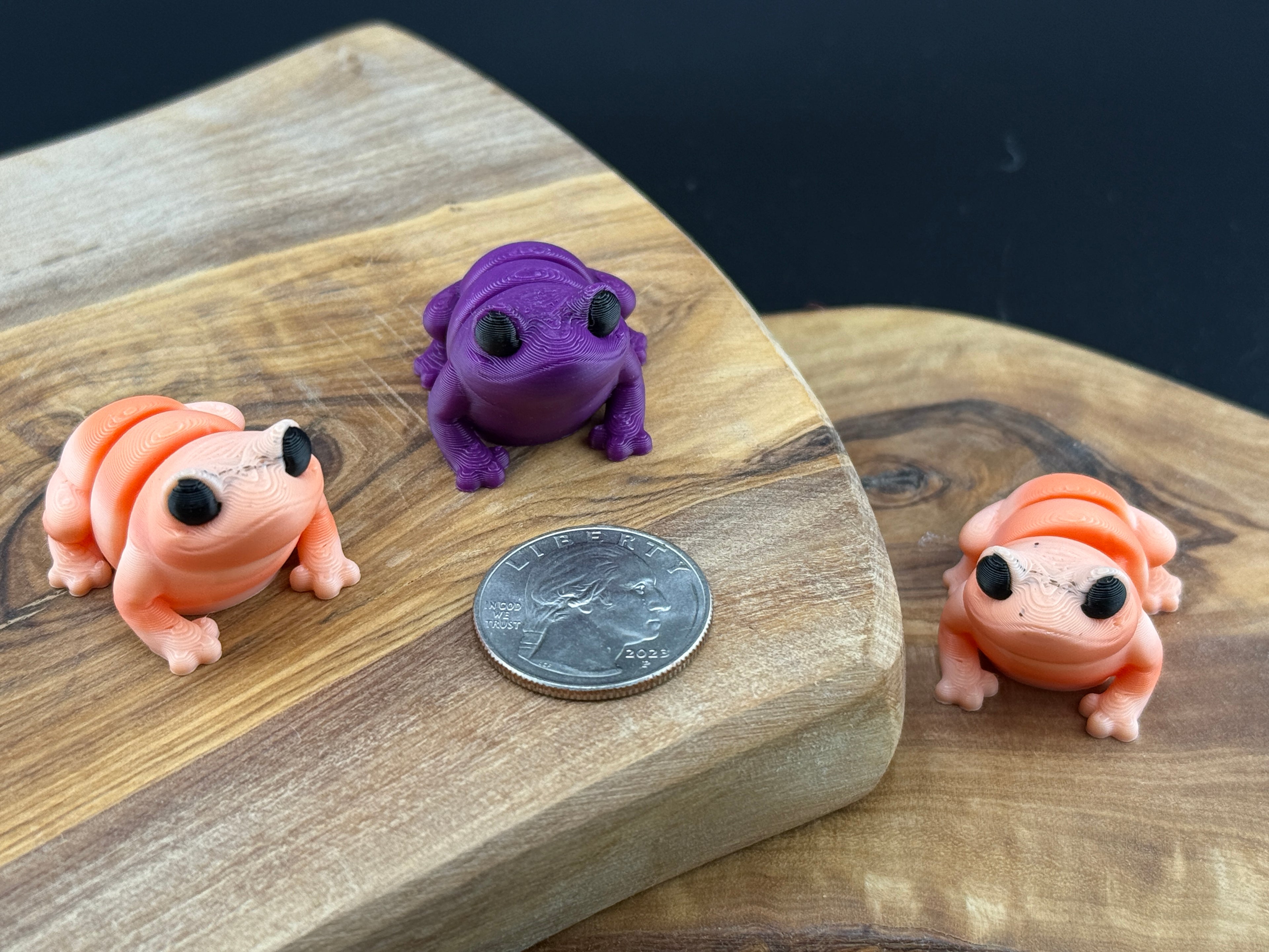 Three small fidget frogs on a wooden surface with a coin for scale.
