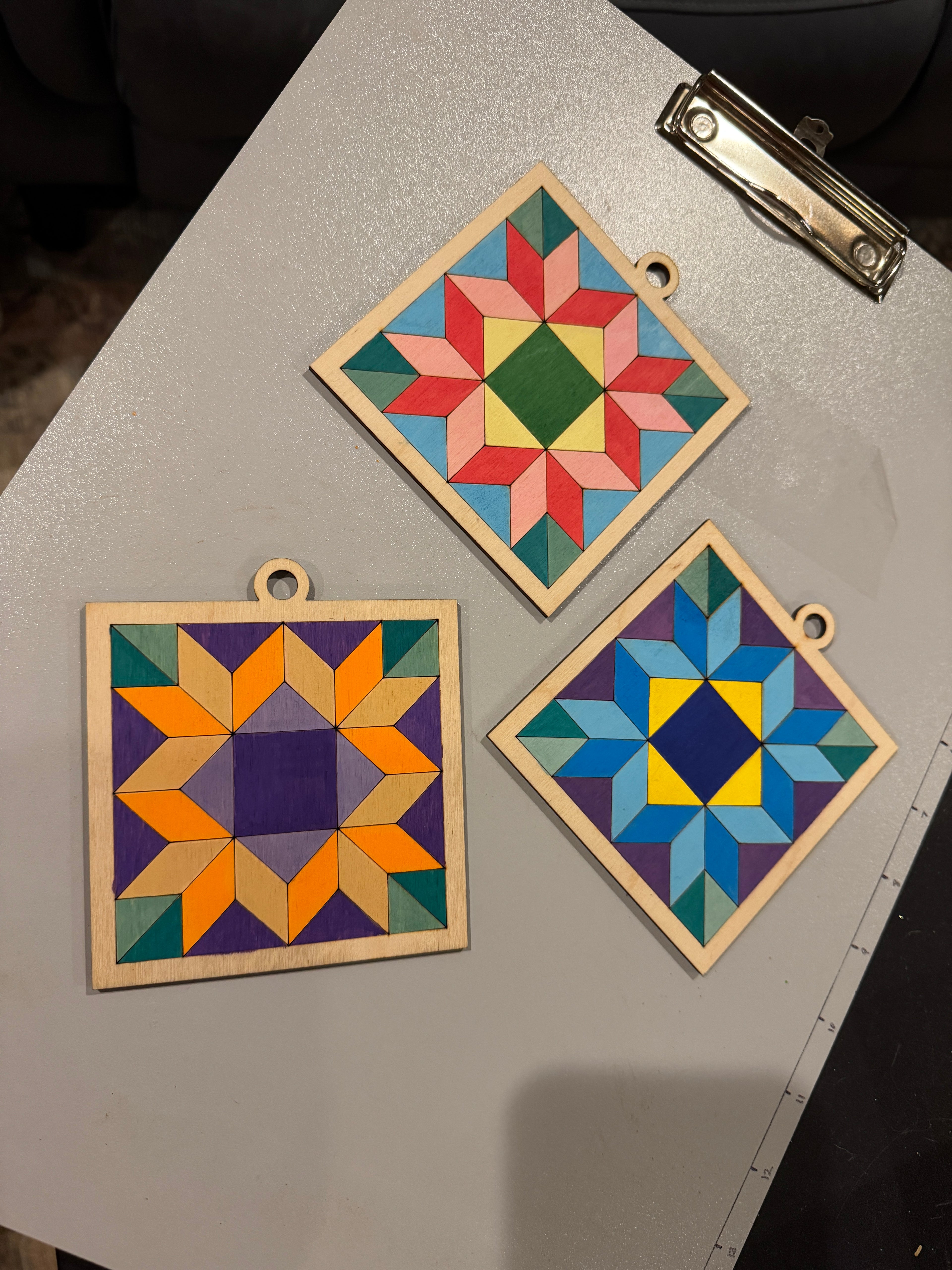 Three colorful wooden square coasters on a gray surface.