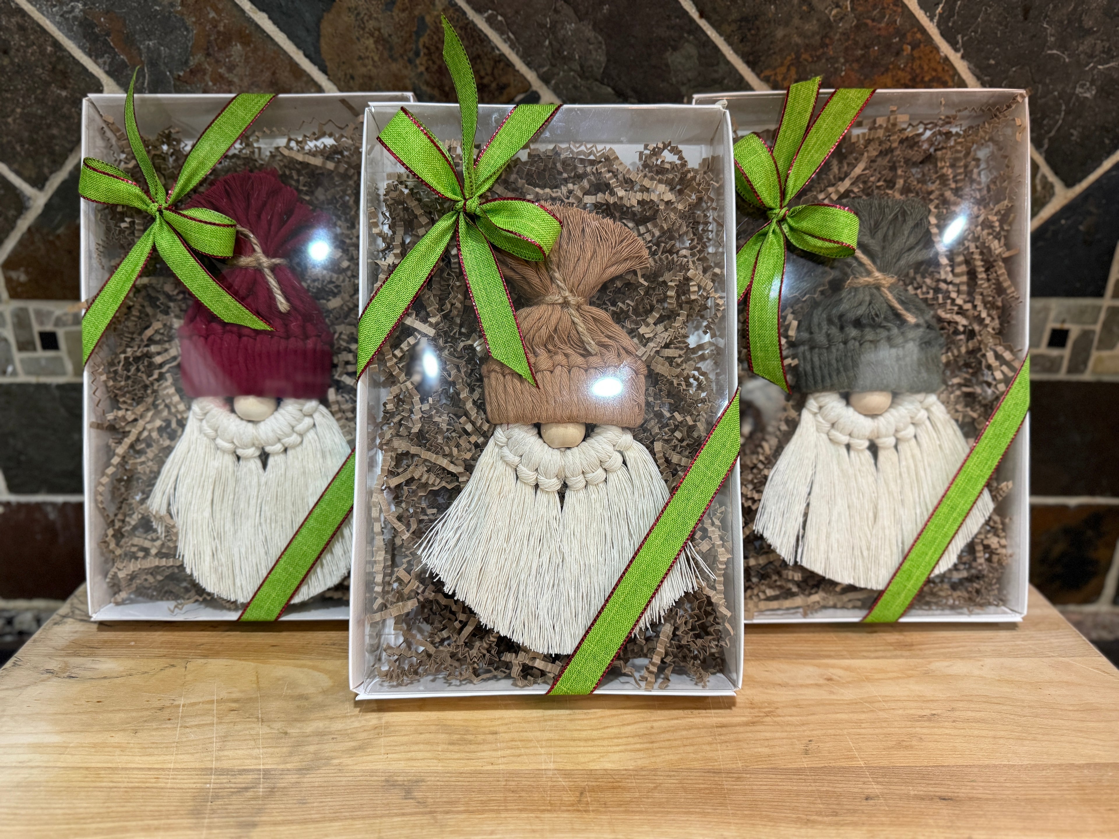 Three decorative gnomes in a box with green ribbons on a wooden surface.