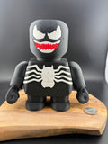 Toy figure resembling a superhero with a black and white costume on a wooden platform.