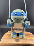 3D printed toy turtle with blue masks and weapons on a wooden surface