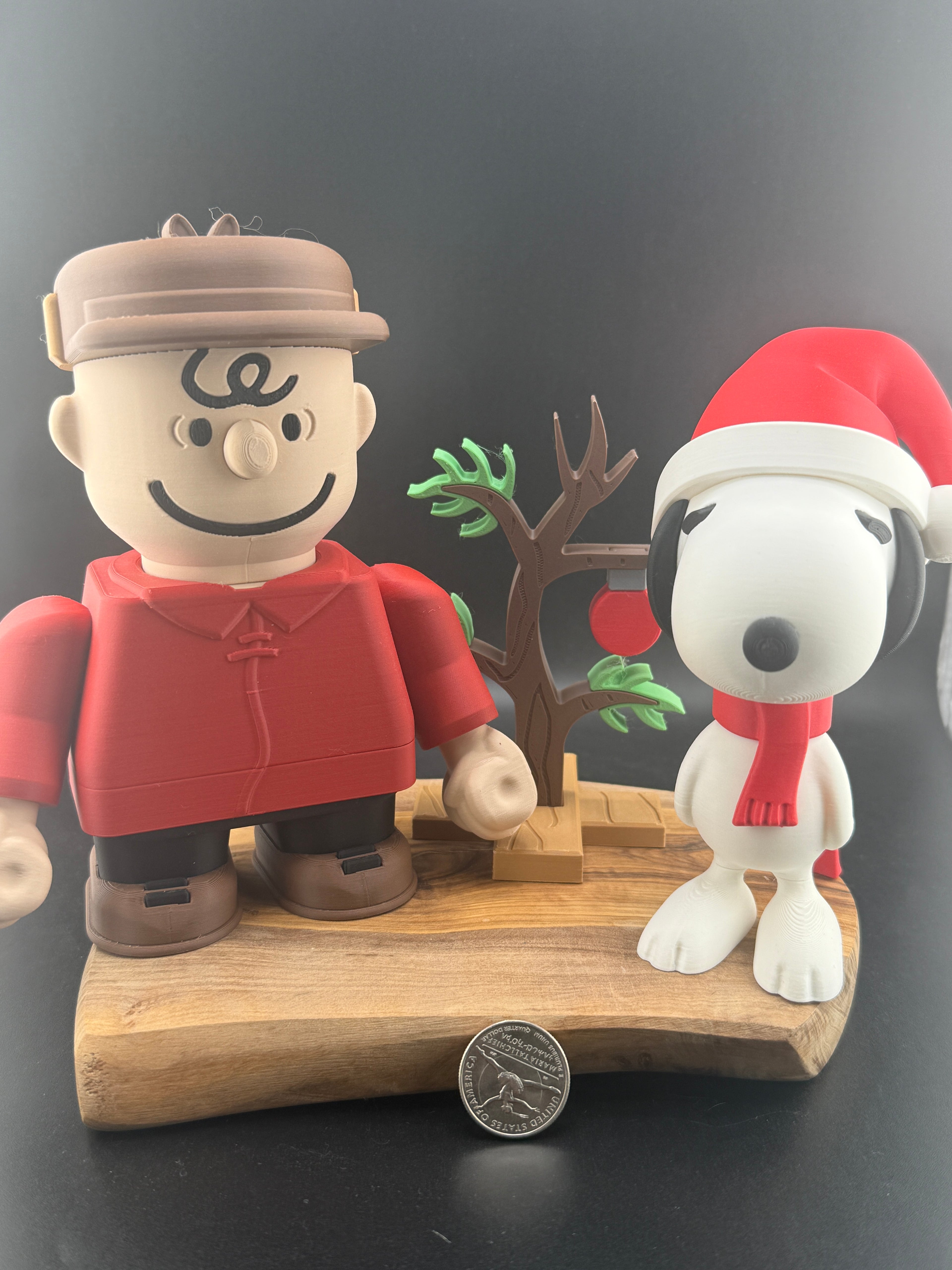 Two figurines, one resembling a boy in a red outfit and cap, and the other resembling a dog in a Santa hat, on a wooden base with a dark background.