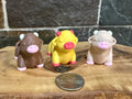 Three small fidget highland cows  on a wooden surface with a coin for scale.
