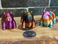 Three colorful 3D-printed hippo fidgets on a wooden surface with a coin for scale.