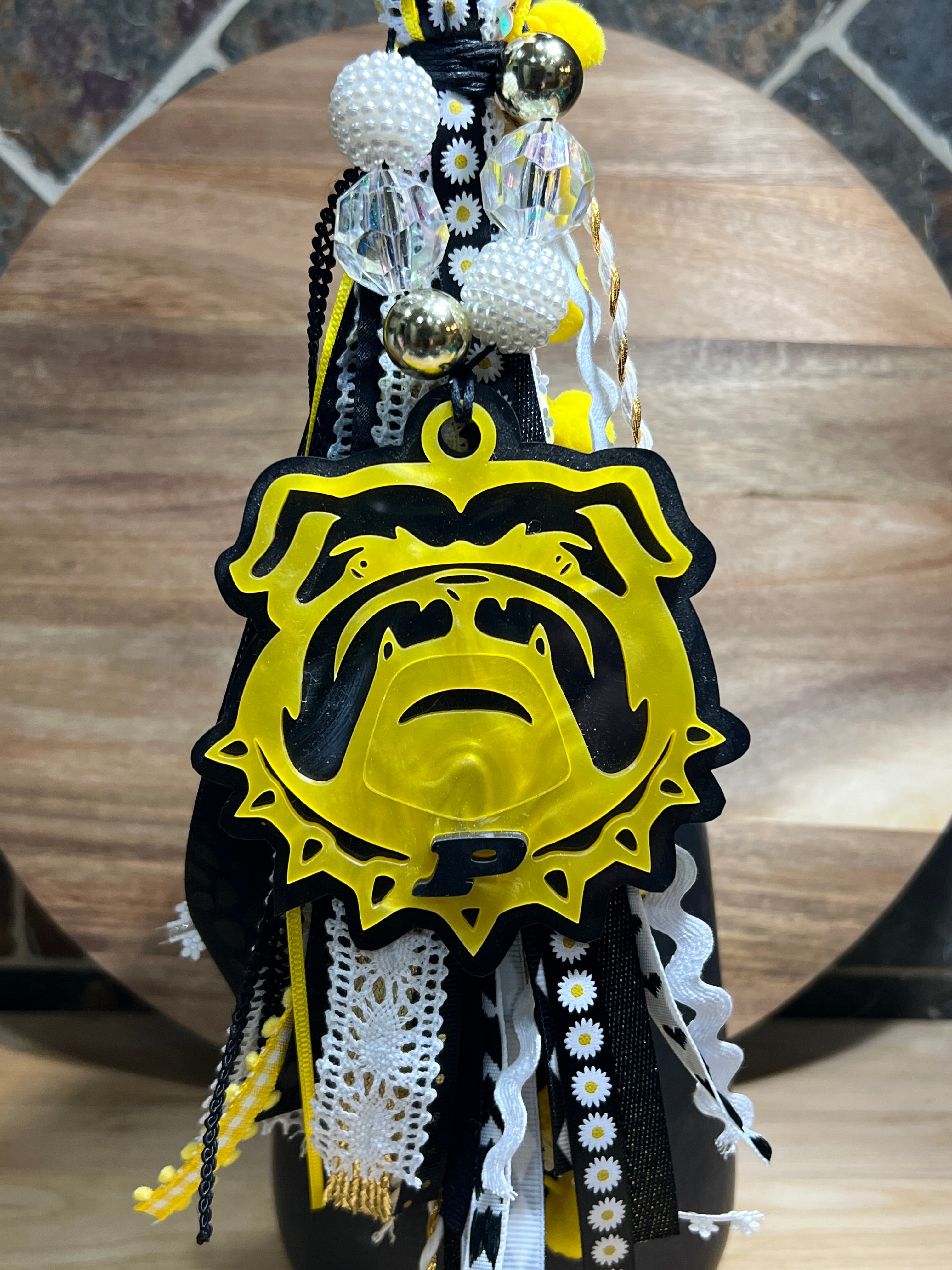 Decorative bag tag with yellow and black ribbon, made of acrylic on a wooden background. 