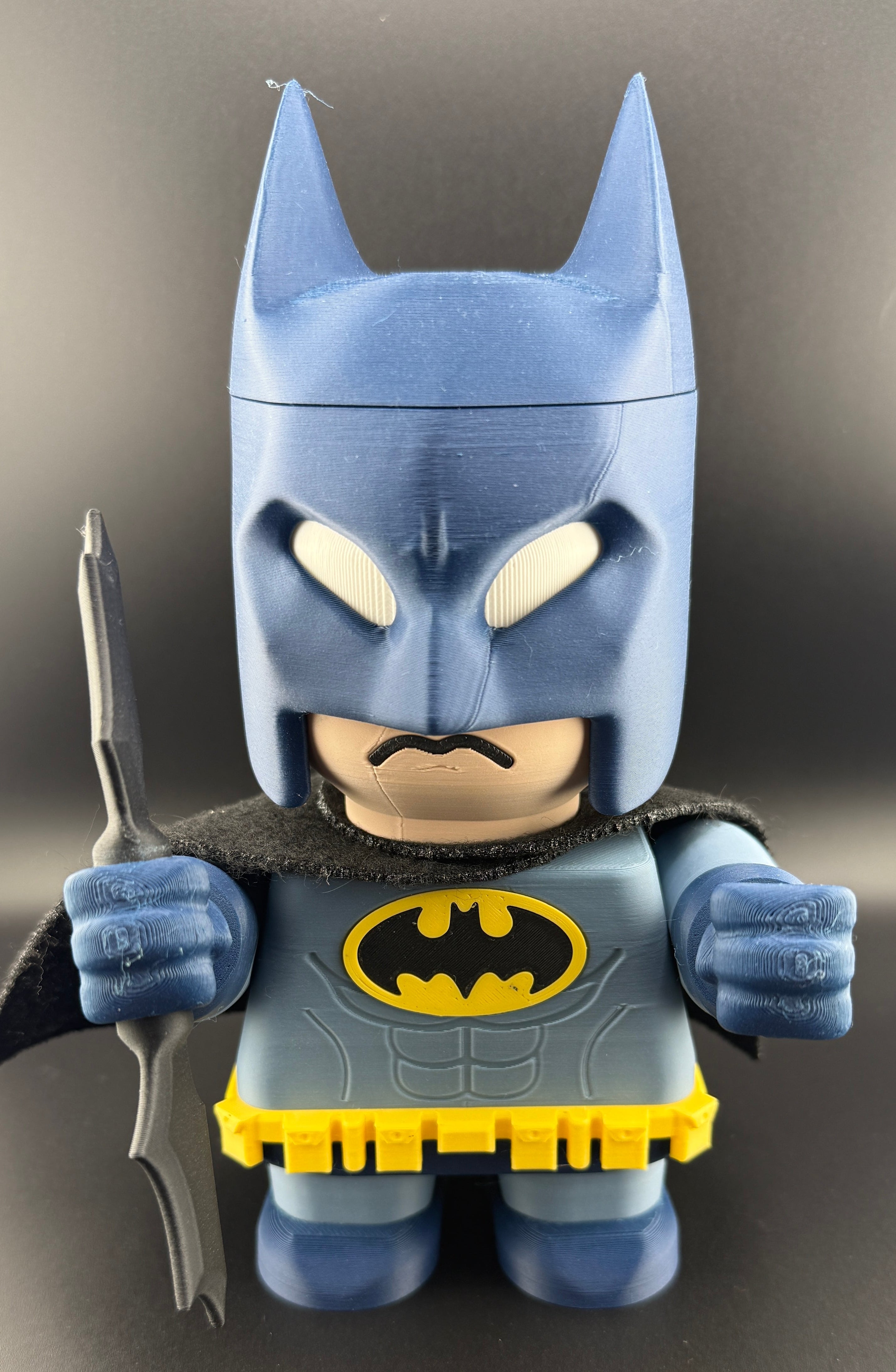 3D bat character with blue suit and yellow bat emblem on a gray background.